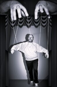 Kognitive Biases. Mann hängt als Marionette an Fäden, die an Händen oberhalb des Mannes festgemacht sind